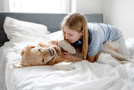 Foto de Chica juega con Golden Retriever en la cama por la mañana en una habitación brillante - Imagen libre de derechos