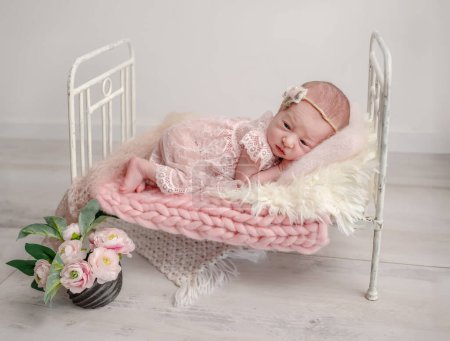 Téléchargez les photos : Nouvelle-née fille en dentelle robe dort dans un petit berceau, capturé en photo professionnelle avec des tons roses - en image libre de droit