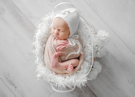 Téléchargez les photos : Fille nouveau-né enveloppé dans une couverture et un chapeau, dormant dans un panier beige, est capturé dans un nouveau-né professionnel Photoshoot - en image libre de droit