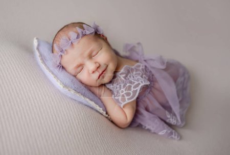 Téléchargez les photos : Nouvelle-née fille en dentelle robe dort et sourit dans son rêve dans des tons lilas Photo - en image libre de droit