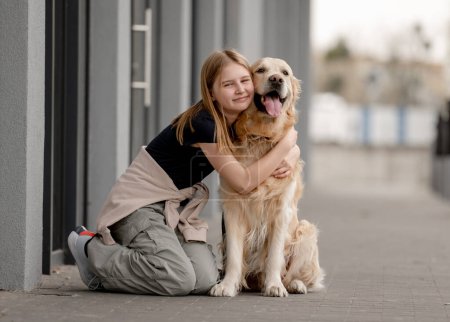 Foto de Chica abraza a Golden Retriever sentada en la calle en verano - Imagen libre de derechos