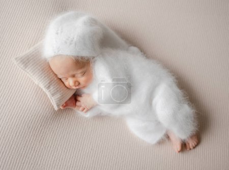 Neugeborenes Baby schläft im weißen Overall beim Fotoshooting im Studio