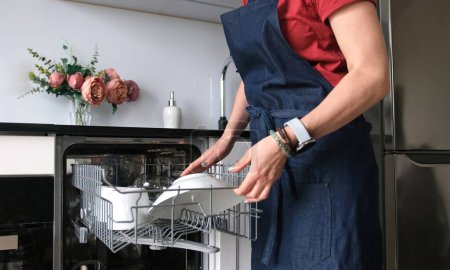 Photo for Girl Retrieves Clean Plate From Dishwasher In Close-Up View - Royalty Free Image