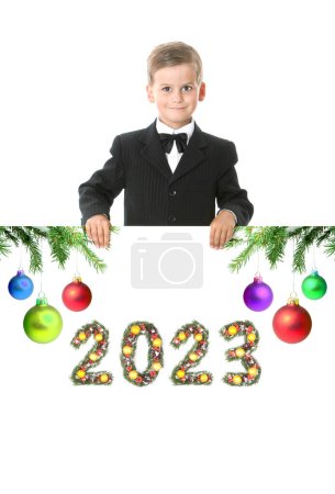 Téléchargez les photos : Garçon tient une affiche de Noël et 2023 numéro faite par les branches de l'arbre de Noël isolé sur fond blanc - en image libre de droit