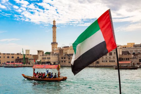 Téléchargez les photos : DUBAI, Émirats arabes unis - 5 AVRIL 2020 : Drapeau des Émirats arabes unis contre Abra - vieux bateau traditionnel en bois sur la baie Creek à Dubaï, Émirats arabes unis - en image libre de droit