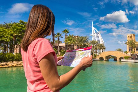 Téléchargez les photos : DUBAI, ÉMIRATS ARABES UNIS - 31 JANVIER 2020 : Une voyageuse heureuse regarde la carte en marchant près de l'hôtel Burj Al Arab et de l'hôtel Madinat Jumeirah à Dubaï, Émirats arabes unis - en image libre de droit