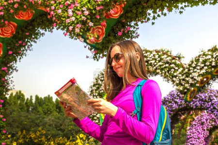 Téléchargez les photos : DUBAI, Émirats arabes unis - 31 JANVIER 2020 : Une voyageuse heureuse regarde la carte en marchant dans le jardin miracle de Dubaï par une journée ensoleillée, Émirats arabes unis - en image libre de droit