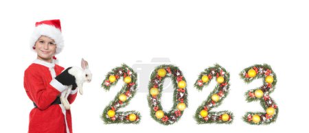 Téléchargez les photos : Nouvel an chinois. Garçon tenant un lapin de Noël et 2023 nombre fait par branches d'arbre de Noël isolé sur fond blanc - en image libre de droit