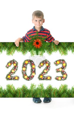 Foto de Niño sostiene un cartel de navidad y 2023 número hecho por ramas de árbol de navidad aisladas sobre fondo blanco - Imagen libre de derechos