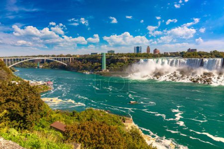 Téléchargez les photos : Vue latérale canadienne des chutes Niagara, des chutes American et du pont international Rainbow par une journée ensoleillée à Niagara Falls, Ontario, Canada - en image libre de droit