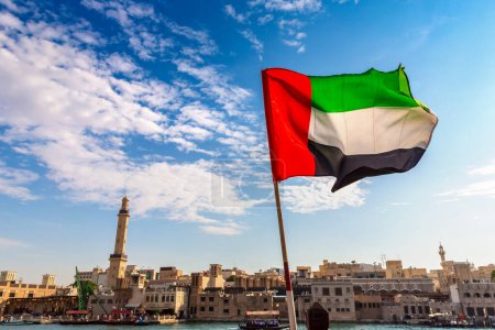 Téléchargez les photos : Focus on a flag of   United Arab Emirates flag against  bay Creek and Grand Bur Dubai Masjid Mosque in Dubai, United Arab Emirates - en image libre de droit