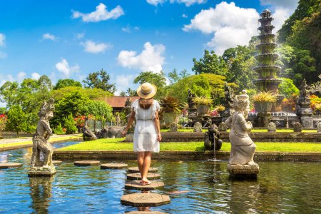 Foto de Mujer viajera vestida de blanco y sombrero de paja en el templo Taman Tirtagangga en Bali, Indonesia en un día soleado - Imagen libre de derechos
