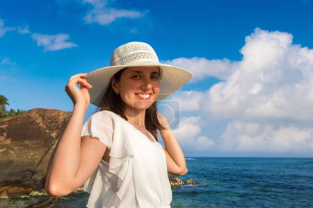 Téléchargez les photos : Portriat de jeune belle femme portant un chapeau et une robe blanche séjournant sur une plage tropicale près de la mer - en image libre de droit