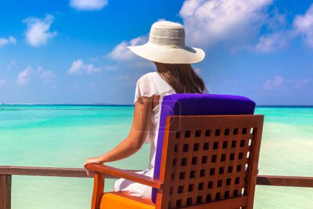 Téléchargez les photos : Belle femme se détendre dans un transat à la plage tropicale de luxe dans une journée d'été ensoleillée - en image libre de droit