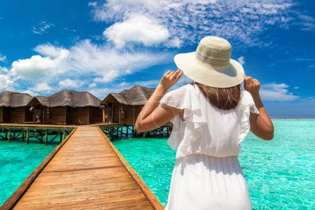 Photo for Beautiful young woman in front of water luxury villas standing on the tropical beach jetty (wooden pier) in Maldives island - Royalty Free Image