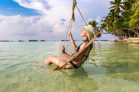 Photo for Beautiful woman is sitting on hammock at luxury tropical beach in a sunny summer day - Royalty Free Image