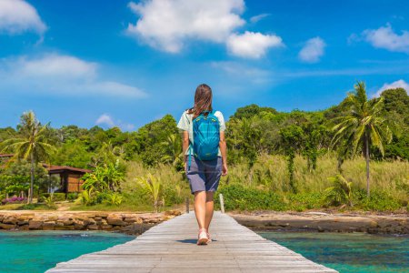 Foto de Mujer viajera caminando en el embarcadero de madera (puente) a la hermosa playa tropical - Imagen libre de derechos
