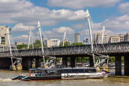 Photo for LONDON, UK - JUNE 17, 2022: An UBER Boat by Thames Clippers on the River Thames and Hungerford Bridge and Golden Jubilee Bridges in London, UK - Royalty Free Image