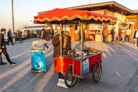 Téléchargez les photos : ISTANBUL, TURQUIE - 10 AVRIL 2022 : Un vendeur turc de rue vend du châtaignier rôti turc traditionnel à Istanbul, en Turquie, par une journée ensoleillée - en image libre de droit