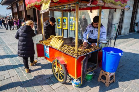 Foto de ISTANBUL, TURQUÍA - 10 DE ABRIL DE 2022: Vendedor turco callejero vende maíz a la parrilla tradicional turco caliente y castaño en Estambul, Turquía en un día soleado - Imagen libre de derechos