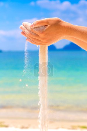 Téléchargez les photos : Sable blanc tombant à travers les mains de la femme à la plage tropicale - en image libre de droit