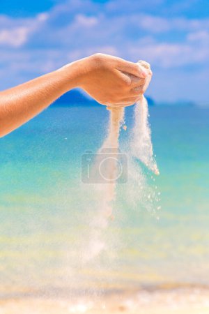 Téléchargez les photos : Sable blanc tombant à travers les mains de la femme à la plage tropicale - en image libre de droit