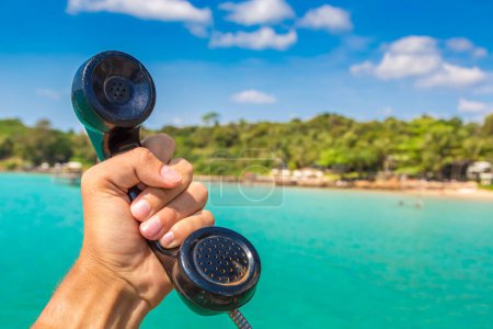 Photo for Male hand holding (handset) retro landline telephone receiver, tropical sea on background - Royalty Free Image