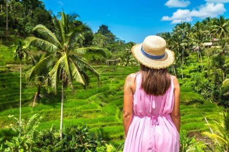 Téléchargez les photos : Une voyageuse vêtue d'une robe rose et d'un chapeau de paille sur la terrasse de riz Tegallalang à Bali, en Indonésie, par une journée ensoleillée - en image libre de droit