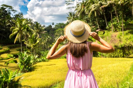 Téléchargez les photos : Une voyageuse vêtue d'une robe rose et d'un chapeau de paille sur la terrasse de riz Tegallalang à Bali, en Indonésie, par une journée ensoleillée - en image libre de droit