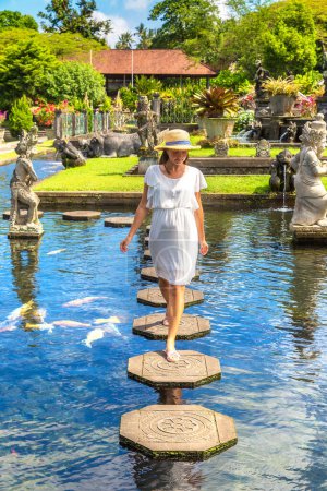 Photo for Woman traveler wearing white dress and straw hat at  Taman Tirtagangga temple on Bali, Indonesia in a sunny day - Royalty Free Image