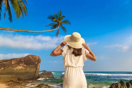 Photo for Portriat of young beautiful woman wearing a hat and white dress staying on a tropical beach near sea - Royalty Free Image
