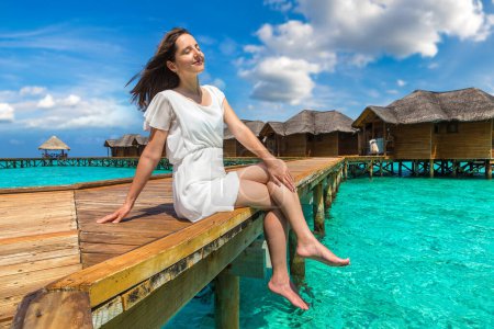 Foto de Hermosa mujer joven en frente de villas de lujo de agua sentado en el embarcadero de playa tropical (muelle de madera) en la isla de Maldivas - Imagen libre de derechos