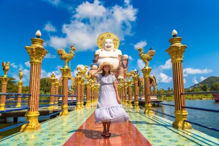 Téléchargez les photos : Femme voyageuse portant une robe bleue et un chapeau de paille à la statue de bouddha géante souriante ou heureuse au temple Wat Plai Laem, Samui, Thaïlande - en image libre de droit