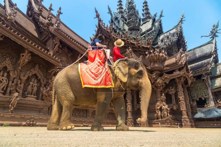 Photo for Tourists ride elephant around the Sanctuary of Truth in Pattaya, Thailand in a summer day - Royalty Free Image