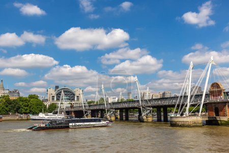 Foto de LONDRES, Reino Unido - 17 de junio de 2022: Un barco UBER de Thames Clippers en el río Támesis y Hungerford Bridge y Golden Jubilee Bridges en Londres, Reino Unido - Imagen libre de derechos