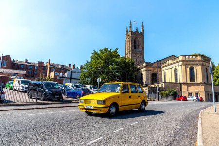Téléchargez les photos : DERBY, Royaume-Uni - 4 SEPTEMBRE 2023 : Voiture de taxi jaune et cathédrale de Derby en arrière-plan par une journée ensoleillée à Derby, Royaume-Uni - en image libre de droit
