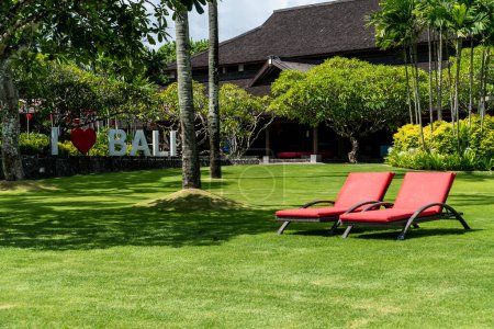 Photo for Two red chairs on a green lawn in a hotel somewhere in Nusa Dua, Bali, Indonesia. Romantic vacation concept - Royalty Free Image