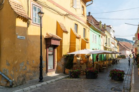 Photo for SIGHISOARA, ROMANIA - august 8, 2019:  Octavian Goga street with street cafes in  Sighisoara, Romania,  in well-preserved old town, listed by UNESCO as a World Heritage Site - Royalty Free Image