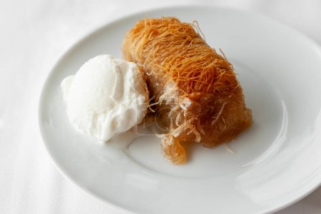 Traditional greek dessert kataifi served with ice cream on a white plate. Classic greek kataifi made with phyllo pastry