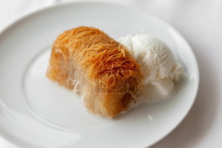 Traditional greek dessert kataifi served with ice cream on a white plate. Classic greek kataifi made with phyllo pastry