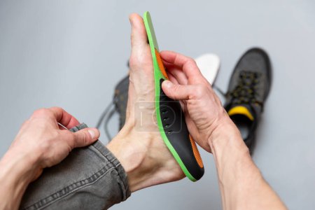 Gros plan des mains de l'homme ajustant les semelles orthopédiques sur un fond gris. Soins de santé et traitement orthopédique et prévention du concept des pieds plats. 
