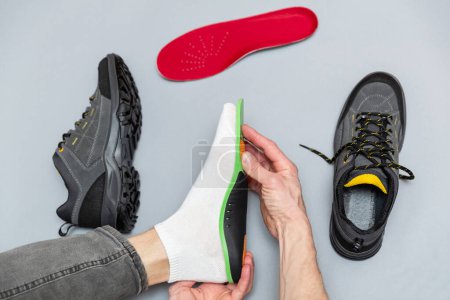 Close up of man hands fitting orthopedic insoles on a gray background. Healthcare and orthopedic treatment and prevention of flatfeet concept. 