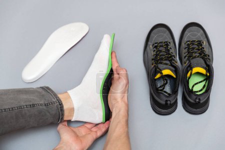 Close up of man hands fitting orthopedic insoles on a gray background. Healthcare and orthopedic treatment and prevention of flatfeet concept. 