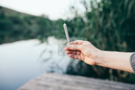 Photo for Cannabis joint man holding in his hand in nature smoking marijuana - Royalty Free Image