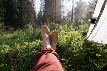 Foto de Salud de los pies, pies en la naturaleza sobre hierba verde, recreación en la naturaleza con una tienda de campaña en verano - Imagen libre de derechos