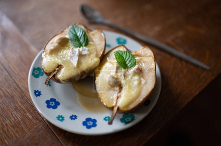 Foto de Postre de pera al horno con queso y una hoja de menta, miel y nueces un plato - Imagen libre de derechos