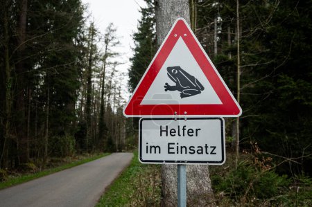 The inscription in German "Help in action" and the sign of a frog near the road