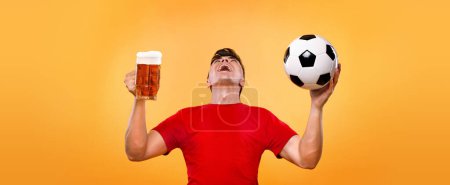 Téléchargez les photos : Fan de sport de football - homme heureux à l'oktoberfest, prendre de la bière et du ballon de football sur fond jaune - en image libre de droit