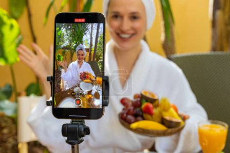 Photo for A blogger girl makes a video review of breakfast at a hotel at holidays. An influencer creates content for social media. Live online broadcast, photography for womens magazines - Royalty Free Image
