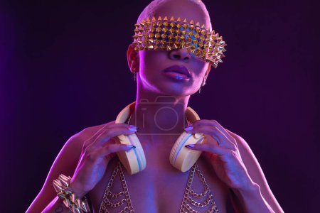 Photo for Girl DJ in neon lights with glasses and headphones. Beautiful woman in violet paint on her face and body. Portrait of sexy TDJ at club party - Royalty Free Image